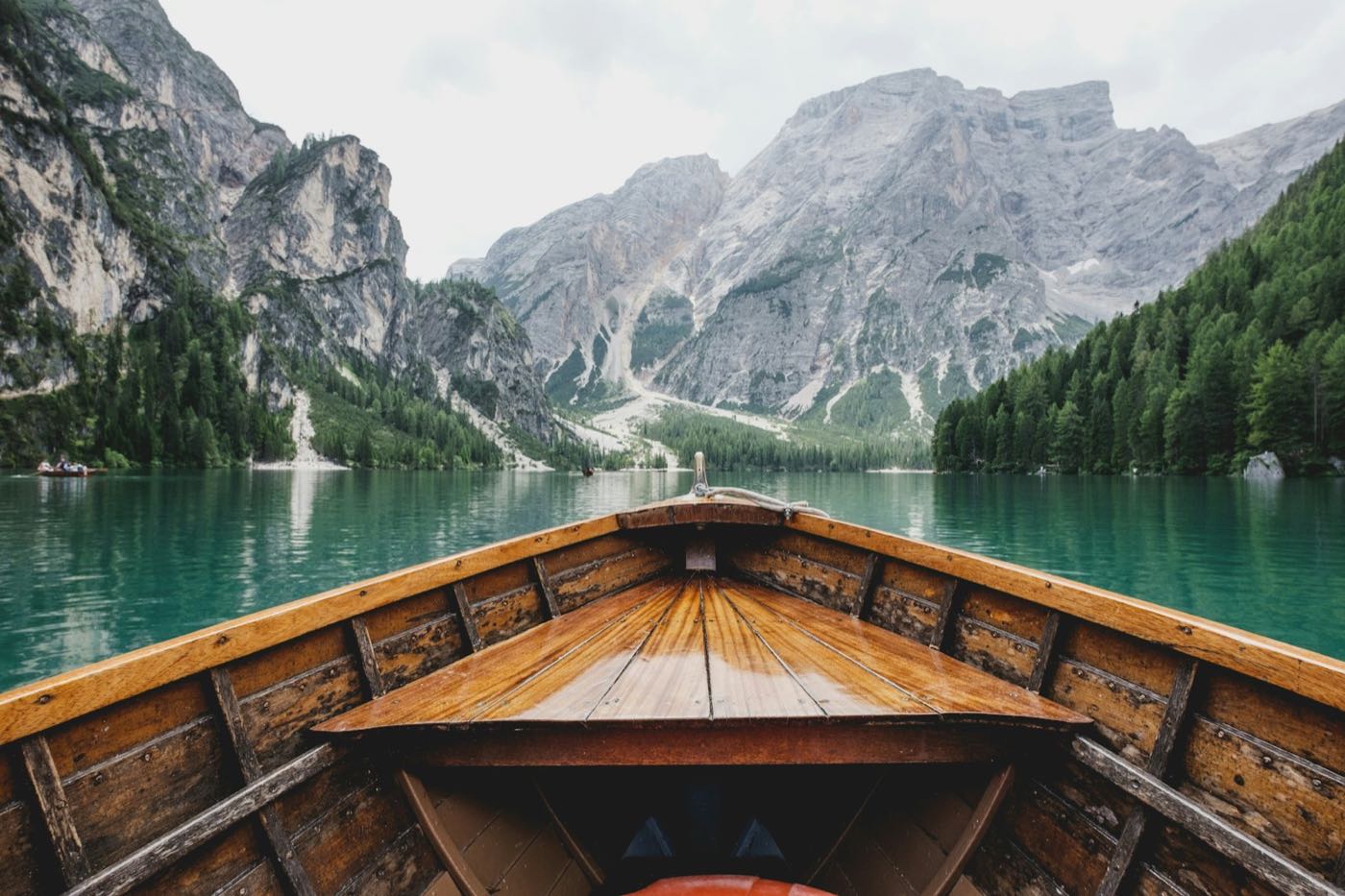 The bow of a wooden boat on a green lake below mountains
